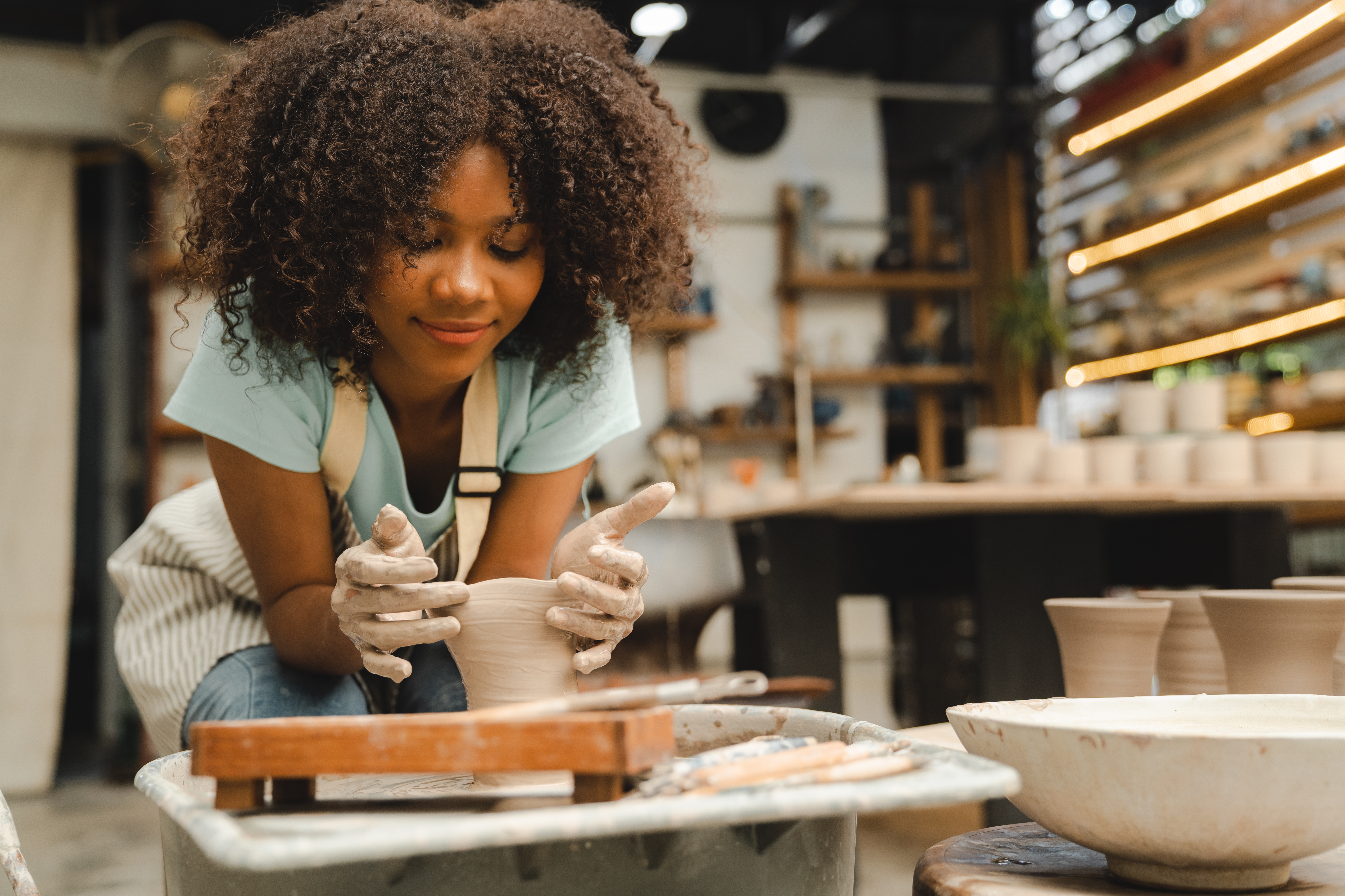 Creative afro American young woman artist molding clay on pottery wheel, Workshop in ceramic studio